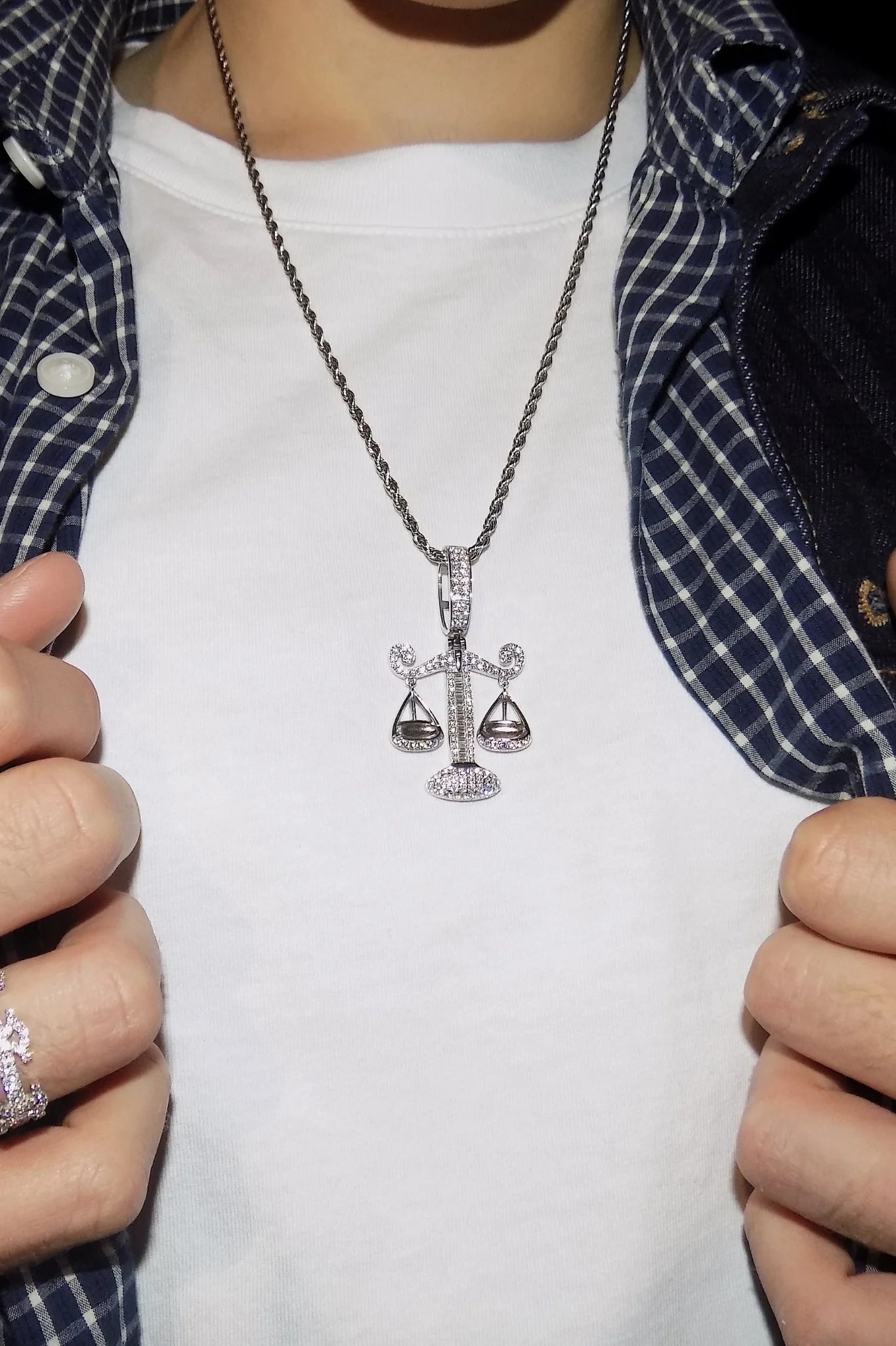 ISOZYGÓS 925 silver balance-scale pendant with moissanite stones worn over a white T-shirt and layered blue shirts — AETHER