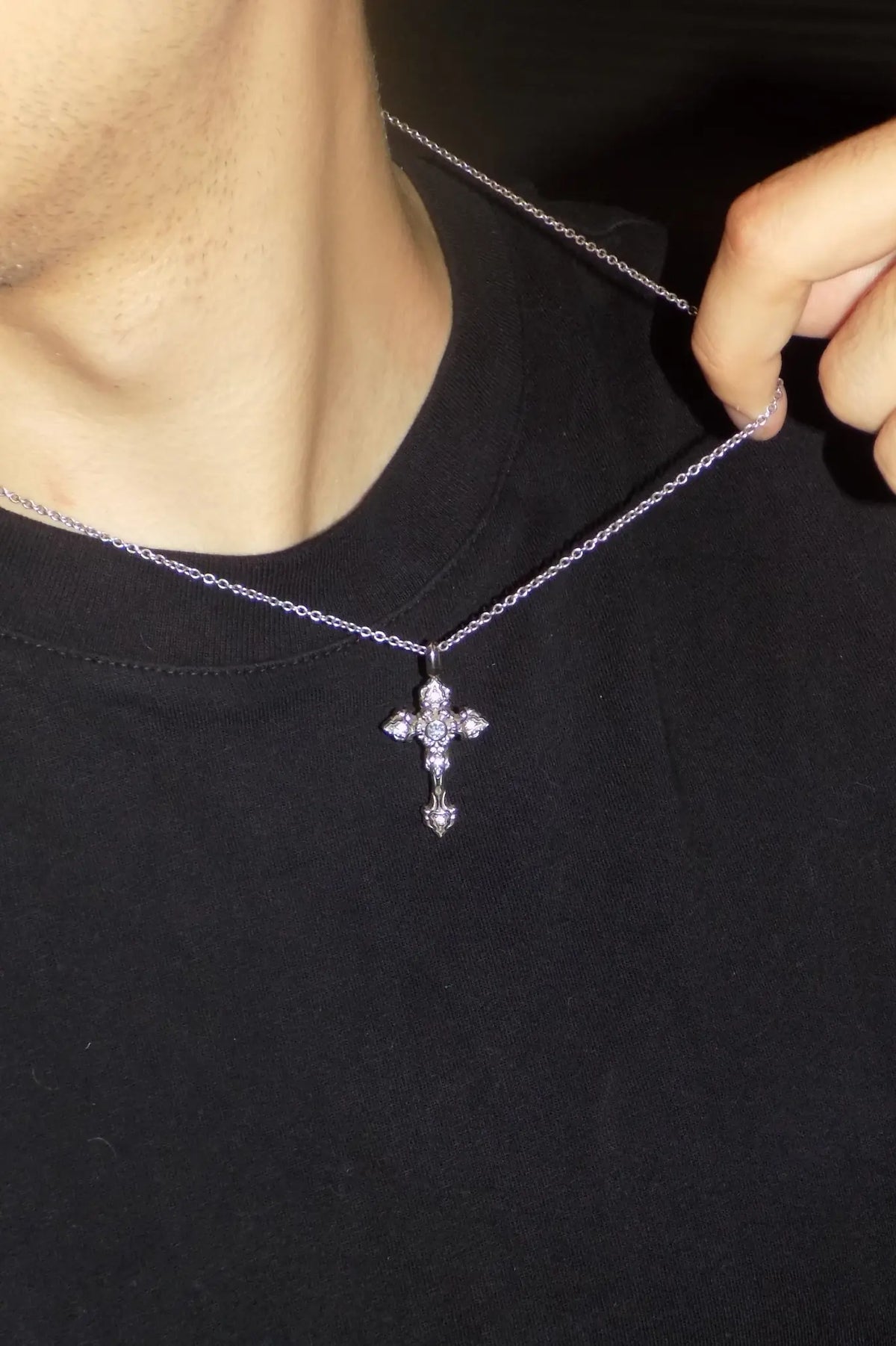 Close-up lifestyle photo of a person wearing the AETHER AMPHIPHÓTOS 925 silver moissanite cross pendant over a black T-shirt, while holding the chain.