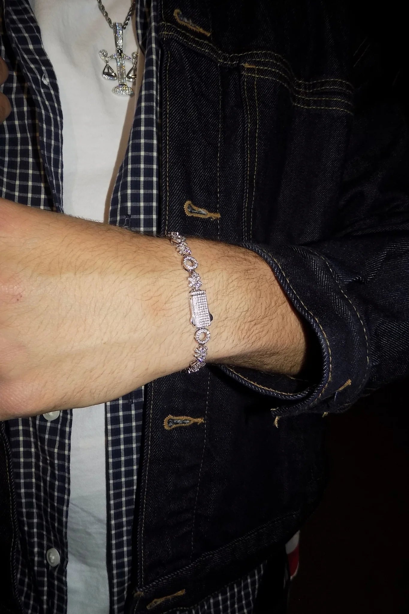 Close-up of a person wearing the ÉLIX 925 silver O-X bracelet with pavé moissanite stones, styled with a dark denim jacket over white and plaid shirts — AETHER